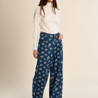 Mulher com calças azuis de padrão floral e camisola branca de manga comprida