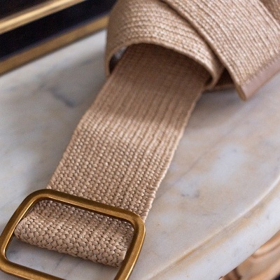Cinto bege em tecido com fivela dourada sobre mesa de mármore