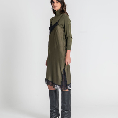 Mulher com vestido verde-oliva e botas pretas, fundo branco