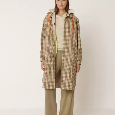 Mulher com casaco xadrez bege, castanho e laranja, calças castanhas e sapatos.