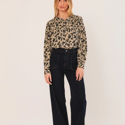 Modelo feminina veste camisa bege com padrão floral preto e calças pretas largas em fundo claro