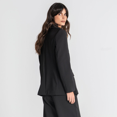 Mulher com conjunto preto de blazer e calças em fundo branco