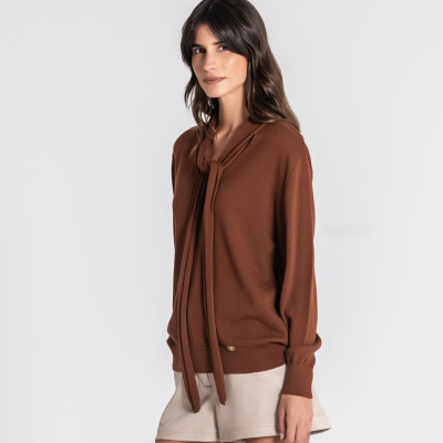 Mulher com camisola castanha de gola com laço e calções bege claro