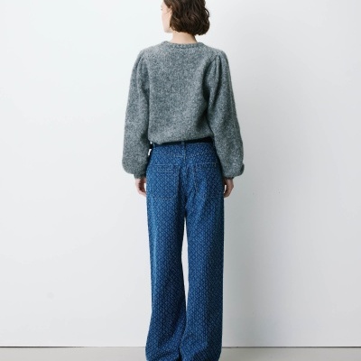 Pessoa de costas com camisola cinzenta de malha e calças largas de ganga azul