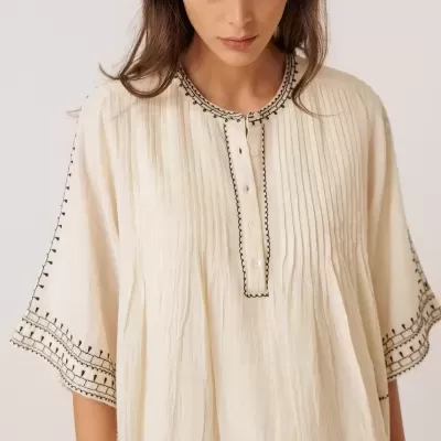 Vestido branco com bordados pretos e botões ao centro, visto de frente em fundo neutro