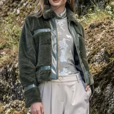 Mulher a usar casaco verde escuro felpudo com detalhes em verniz e calças bege em ambiente exterior com rochas e vegetação