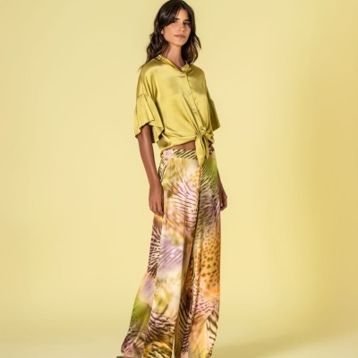 Mulher com camisa de cetim verde e calças largas estampadas em fundo amarelo