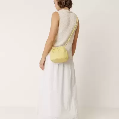 Mulher com colete creme, saia branca bordada, sandálias bege e bolsa tiracolo amarela