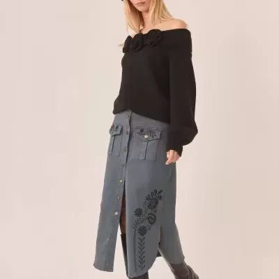 Mulher com camisola preta de ombros descobertos e saia azul com bordados