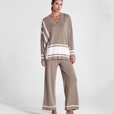 Conjunto bege de camisola e calças largas com riscas brancas, mulher com cabelo preso e sapatos brancos de salto