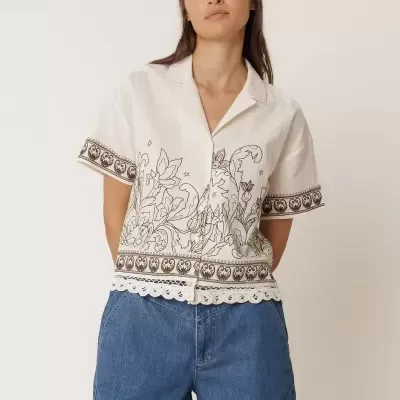 Mulher a usar camisa branca com padrão floral castanho e calções de ganga azuis.