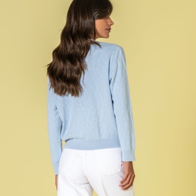 Mulher de cabelo castanho comprido com camisola azul clara e calças brancas