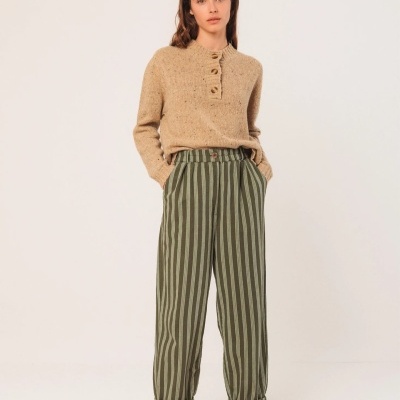 Mulher com camisola bege de malha e calças de riscas verdes e cinza.