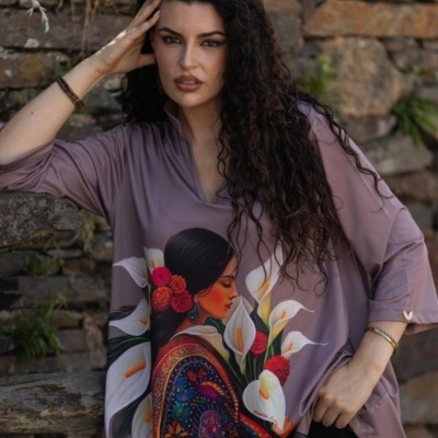 Blusa oversized roxa com estampa de mulher com flores, modelo com cabelo encaracolado, parede de pedra ao fundo