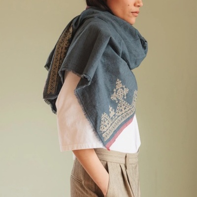 Lenço cinza-azulado com bordado bege e detalhe vermelho usado por pessoa de camiseta branca e calças bege