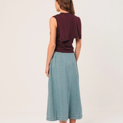 Mulher de costas com blusa vinho, saia azul clara e sapatos estampados