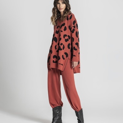 Conjunto feminino com camisola oversized laranja com manchas pretas, calças largas laranja e botas pretas em fundo branco.