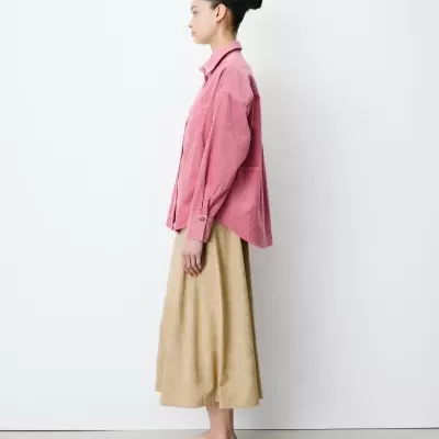 Mulher de perfil com camisa rosa de veludo cotelê e saia bege, sapatos rasos bege