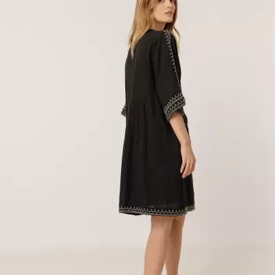 Vestido preto com bordados brancos e textura enrugada, visto de costas