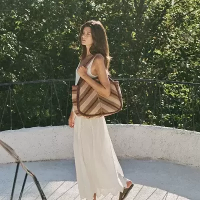 Mulher com vestido branco e bolsa listrada num varandim exterior
