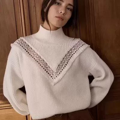 Camisola branca de malha com renda e calças castanhas em fundo de porta de madeira.