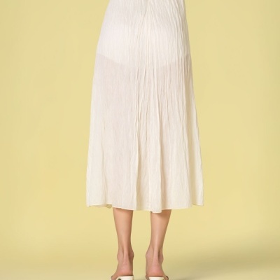 Saia midi branca plissada vista de costas num fundo amarelo claro.