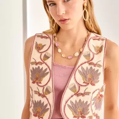 Colete bordado floral bege sobre top rosa claro e saia bege texturizada