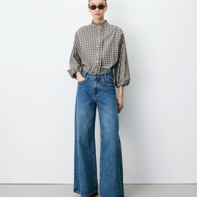 Mulher vestindo blusa xadrez, jeans e óculos escuros em fundo branco.