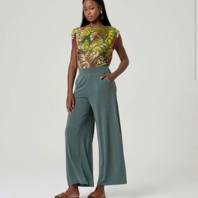Mulher com blusa estampada de folhas e calças largas verdes, sandálias castanhas