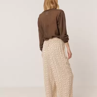 Mulher de costas com camisola castanha e calças largas bege com padrão floral