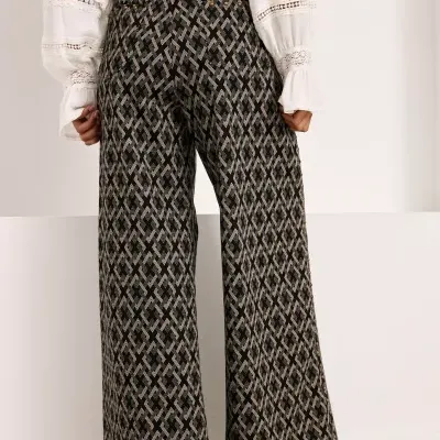 Calças pretas largas com padrão geométrico bege, blusa branca com rendas, sapatos castanhos.