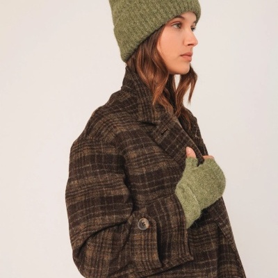 Mulher com casaco xadrez castanho e preto, gorro verde de malha e luva verde de dedo polegar à vista