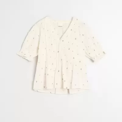 Blusa creme com padrão de pequenos pontos, mangas curtas e botões frontais