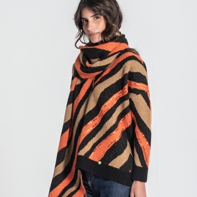 Mulher com camisola de malha riscada preta, laranja e castanha com cachecol e calças de ganga azul