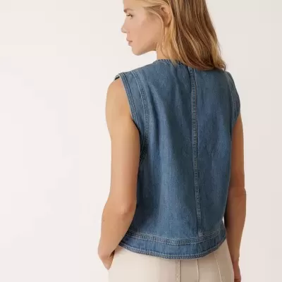 Mulher de costas com colete de ganga azul e calças bege claras