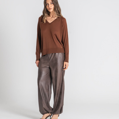 Mulher com camisola castanha de malha e calças cinza acetinadas largas.