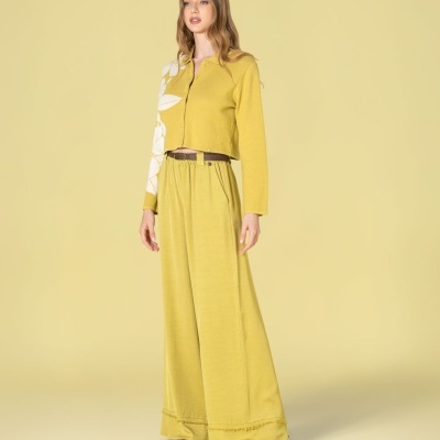 Mulher com conjunto amarelo, casaco com padrão branco na manga e calças largas amarelas