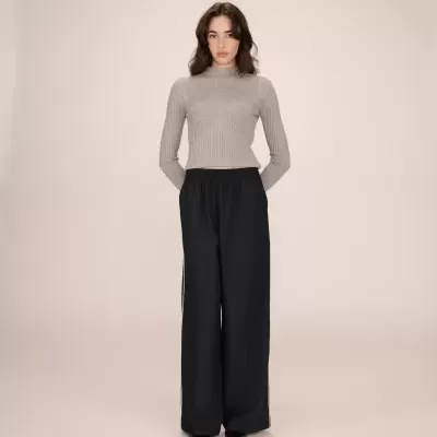 Pessoa com camisola cinza de malha e calças largas pretas num fundo bege claro