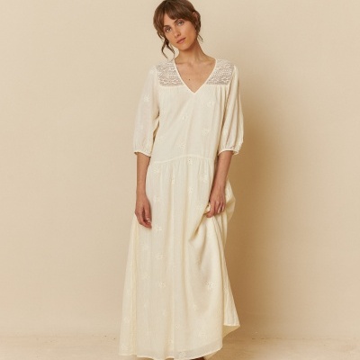 Vestido longo branco com detalhes em renda e mangas 3/4, usado por mulher em fundo neutro.
