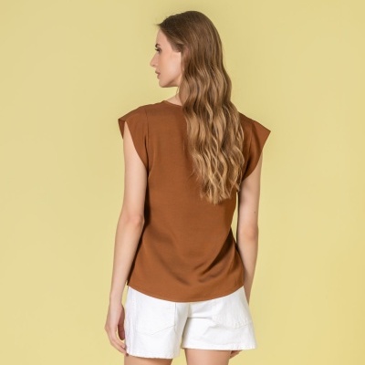 Mulher de costas com blusa castanha e calções brancos em fundo amarelo