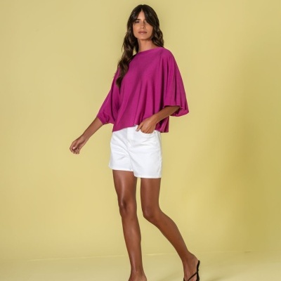 Mulher com camisola rosa fúcsia, calções brancos e sandálias pretas, fundo amarelo claro.