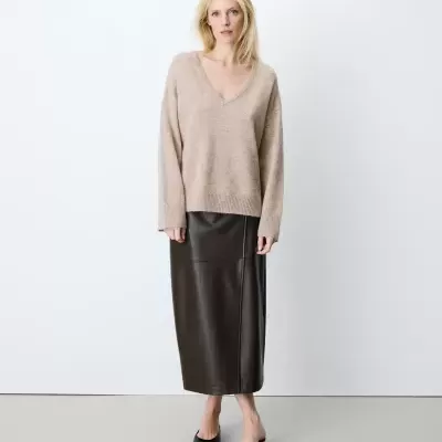 Mulher com camisola bege de malha e saia midi de pele preta