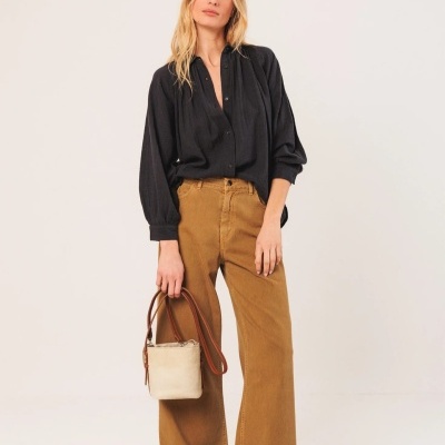 Mulher com camisa preta, calças castanhas largas e bolsa bege com alças castanhas