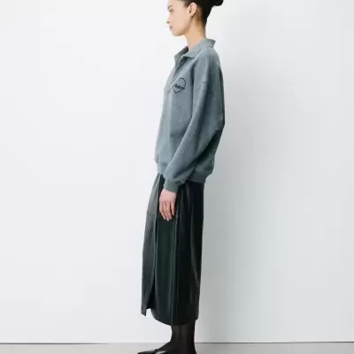 Mulher vista de perfil com roupa cinzenta e preta contra fundo branco