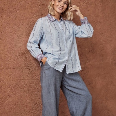 Camisa azul clara com riscas e calças largas cinza em fundo castanho.