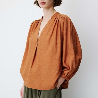 Blusa laranja com gola redonda e mangas abalonadas, usada com calças verdes