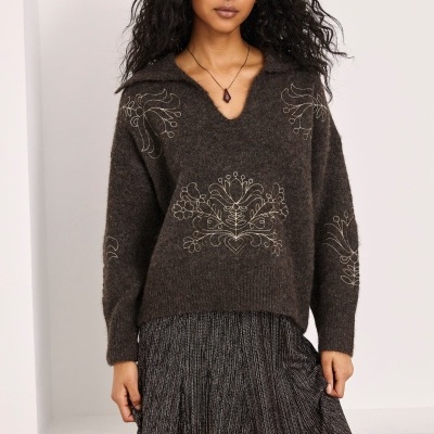 Mulher com camisola castanha de malha com bordado floral e saia longa cinzenta plissada