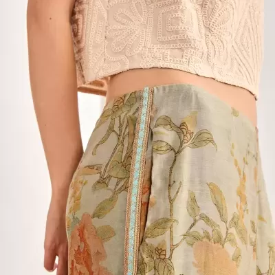 Top cropped bege com padrão geométrico em relevo e saia com estampa floral em tons de verde e laranja com faixa azul e dourada na lateral.