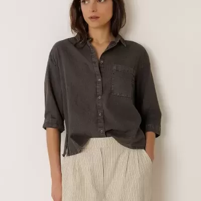 Mulher com camisa cinzenta escura e calças brancas às riscas finas pretas