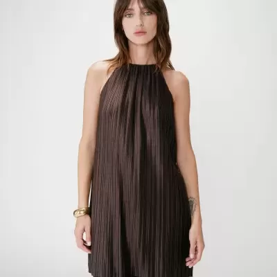 Mulher veste túnica preta plissada e calças largas plissadas.